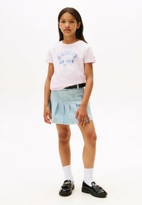 Camiseta de manga corta rosa con impresión azul "Tommy Hilfiger New York City", combinada con una falda plisada azul clara y mocasines negros.