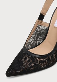 Chaussure slingback noire à bout pointu, avec semelle intérieure beige et bordure noire.