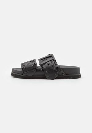 Sandalias tipo slide negras con dos correas de hebilla, decoradas con tachuelas en forma de pirámide, plantilla texturizada y suela plana de goma. Diseño minimalista.
