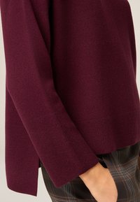 Bordeauxkleurige gebreide trui met wijde mouwen en structuurstof; heeft zijslitsen aan de zoom voor extra stijl en comfort.