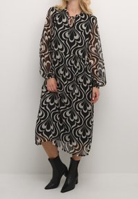 Robe midi noire et beige à motifs, avec manches longues en voile transparent et encolure à ouverture en goutte d'eau. Le tissu a une texture fluide ; présente une taille froncée.