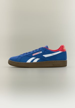 Blauwe Reebok sneaker met witte strepen, rode hieltab en bruine zool, weergegeven in zijaanzicht op een neutrale achtergrond.