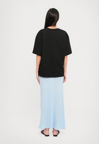 Čierne oversized tričko s krátkymi rukávmi v kombinácii so svetlomodrou, dlhou a voľnou sukňou a čiernymi šľapkami.