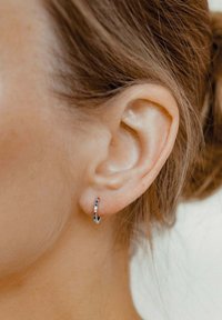 Boucle d'oreille en argent avec des accents de pierres précieuses multicolores, présentant une surface lisse et réfléchissante et un design courbé. Portée sur une oreille.