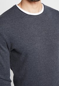 Felpa grigia in maglia con una texture liscia, dotata di un collo a girocollo bianco, maniche lunghe e una vestibilità comoda.