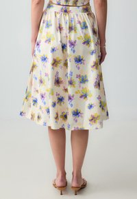 Blumiger Midi-Rock mit einem cremefarbenen Hintergrund, auf dem blaue, gelbe und rosa Blumen printiert sind. Er besteht aus leichtem Material und hat einen elastischen Bund.