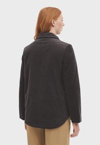 Dunkelgraue Cord-Jacke mit Schalkragen, langen Ärmeln und abgerundetem Saum, die über eine strukturierte Oberfläche und ein lässiges Design verfügt.