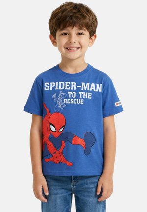 Garçon souriant portant un t-shirt bleu Spider-Man avec le texte « Spider-Man to the rescue » et un graphisme, associé à un jean en denim bleu.