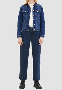 Džínová bunda tmavě modré barvy s dvěma náprsními kapsami, zapínáním na knoflíky a klasickým límečkem. Doplněná o široké kalhoty s vysokým pasem v tmavě modré džínovině.