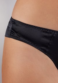 Czarne satynowe majtki bikini o gładkiej teksturze, z płaskim pasem i zygzakowymi szwami wzdłuż brzegów.
