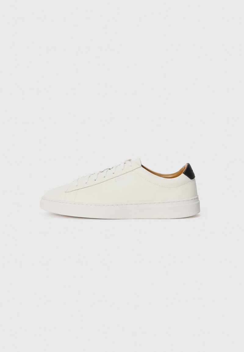 Hvide sneakers med overdel i glat læder, rund tå og flad sål. Sort accent ved hælen, med tonede snører og minimal branding.
