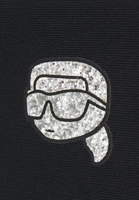 Tessuto nero con un design grafico argentato in paillettes che rappresenta un volto con occhiali da sole e un contorno stilizzato.