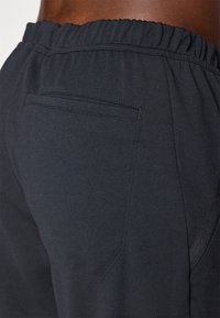 Schwarze Sportshorts aus strukturiertem Stoff, ausgestattet mit einem elastischen Bund und einer einzelnen Gesäßtasche mit einem dezenten Nahtdetail.