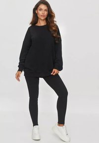Czarny sweatshirt z długim rękawem i ribbowanym dołem, w zestawie z czarnymi legginsami. Materiał wydaje się miękki i teksturowany. Włożony z białymi sneakersami.