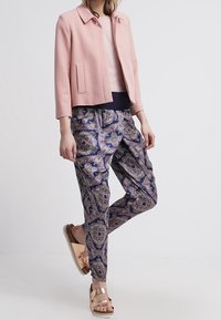 Light pink cropped jacket, navy top, patterned loose trousers in blue, gold, and beige, with flat metallic sandals.