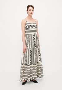 Rochie maxi cu modele geometrice alb-negru, având un corset ajustat, bretele subțiri și o fustă fluidă cu volane. Textură de țesătură netedă.