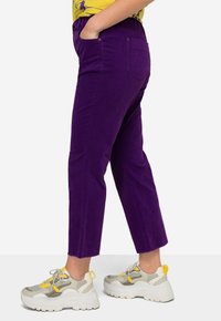 Lila kordjeans med cropped passform och avslappnad stil, med resårmidja och bakfickor, tillsammans med klumpiga vita sneakers.