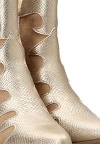 Botas de tobillo metálicas doradas con un patrón de piel de serpiente texturizado, que presentan detalles recortados y un acabado de ante suave en los laterales.