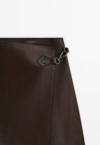 Jupe en cuir marron foncé avec une boucle argentée et un détail en boucle à la taille, présentée sur fond blanc.