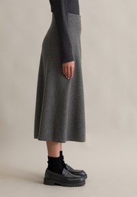 Fustă midi din lână gri, cu un talie înaltă, textură netedă și o siluetă evazată, asortată cu mocasini negri și șosete cu dungi.