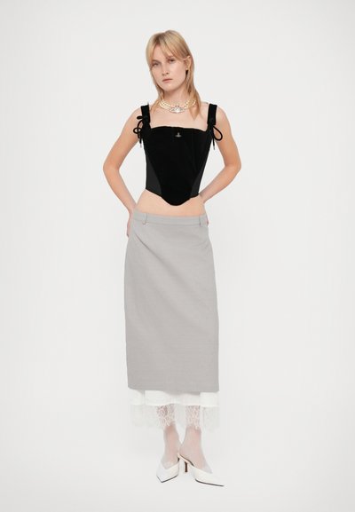 Γυναίκα με μαύρη βελούδινη αμάνικη μπλούζα, γκρι μίντι φούστα με λευκή δαντελένια βάση, λευκές διάφανες καλσόν, λευκά τακούνια και ένα κολιέ με πέρλες.
