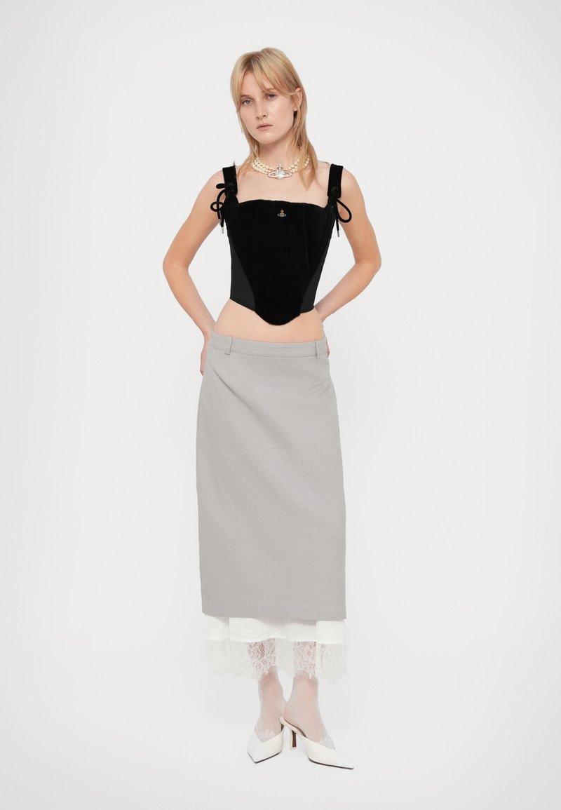 Kvinna klädd i svart sammetsärmlös topp, grå midiklänning med vit spetskant, vita genomskinliga tights, vita klackskor och ett pärlhalsband.