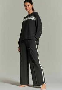 Zwart loungewear-set met een cropped sweatshirt met witte branding en wijde broek met zijkantenstrepen. Geweven stof, relaxte pasvorm.