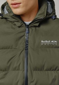 Zeleni jakna s podstavom i zatvaranjem na zip, koja ima kapuljaču i logotipe "Red Bull Racing" i "Pepe Jeans" sprijeda.