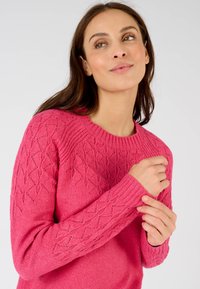 Maglione rosa a maglia con un motivo a diamante testurizzato sulle maniche e colletto a coste. Il materiale sembra morbido e leggero.