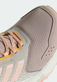 Lightweight athletic shoe featuring a textured light gray upper, mesh detailing, pink accents, and orange laces. Rubber sole with patterned grip.