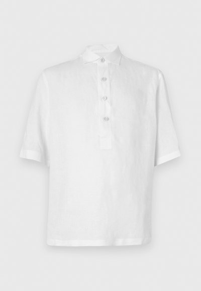 Fehér rövidujjú pólóing, amely lenből készült. Gombos kapoccsal, klasszikus gallérral és laza szabással rendelkezik. Simább, könnyű textúrával.