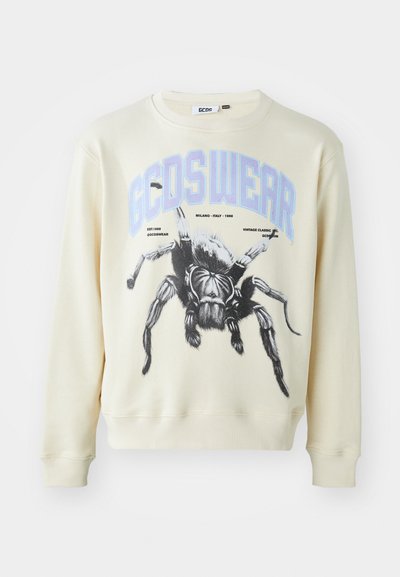 Krém színű pulóver, nagy fekete pók grafikával és kék "GCDS WEAR" felirattal. Bordázott mandzsetták és alsó rész, valamint kerek nyakú kialakítás.