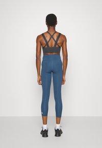 Träningsoutfit som innehåller en mörkgrå sportbh med korsrygg och högmidjade blå leggings med en slät och fin textur samt subtila sömnadsdetaljer.