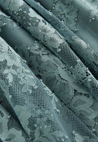 Tissu en dentelle bleue avec motifs floraux et petits points en relief, plié en plis doux.