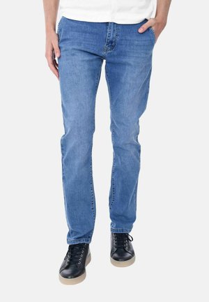 Jeans in denim azzurro chiaro con taglio dritto, cinque tasche e un leggero effetto sbiadito. Abbinati a scarpe da ginnastica nere con suole bianche.