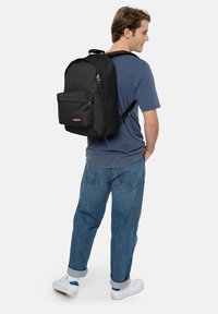 Schwarzer Rucksack mit einem schlanken Design, ausgestattet mit einer vorderen Reißverschlusstasche, verstellbaren Trägern und strapazierfähigem Material, getragen auf dem Rücken einer Person.