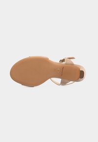 Μπεζ σανδάλι ψηλοτάκουνο με υφασμένα λουριά και αγκράφα στον αστράγαλο, εμφανιζόμενο από την πλευρά της σόλας με εμφανή τα σήματα της μάρκας και του μεγέθους.