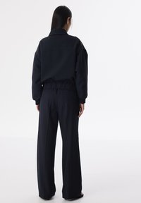 Veste oversize bleu marine avec un col et une taille froncée, associée à un pantalon à jambe large, texture lisse, design minimaliste.