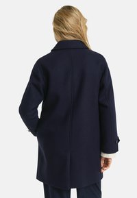 Marineblauwe wollen jas met een gestructureerde kraag, rechte snit en twee zijzakken, voorzien van knoopaccenten op de mouwen en een gladde textuur.