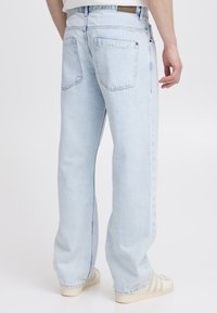Jeans azzurri chiaro a gamba larga con vita alta, caratterizzati da due tasche posteriori. Il tessuto ha una texture liscia e una finitura denim casuale.