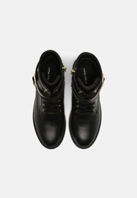 Bottes cheville en cuir noir avec ferrures dorées, bout arrondi, laçage avant et design avec revers. Semelle texturée pour une meilleure adhérence et stabilité.
