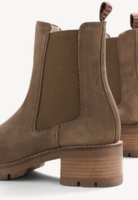 Bottes cheville en daim marron avec des panneaux latéraux élastiques texturés, des talons en bois empilés et des languettes à rayures rouges et blanches.