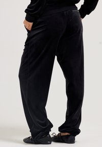 Zwarte, zachte fluwelen loungebroek met een ontspannen pasvorm, elastische boorden en zijzakken. Kenmerkt een ritsaccent op de achterkant van de taille.