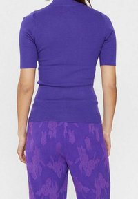 Kortärmad lila ribbad topp med hög krage, parat med matchande lila byxor med texturerade blommönster.