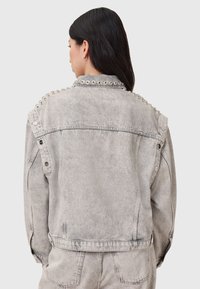 Giacca in denim grigia con una vestibilità rilassata, dotata di dettagli con borchie lungo le spalle e chiusure a bottoni a pressione. Tessuto testurizzato.