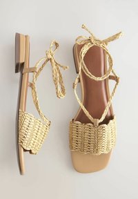 Geweven stro sandalen met een brede band, lichtbruine kleur. Kenmerkt een platte rubberen zool en gevlochten enkelbanden voor een veilige pasvorm.
