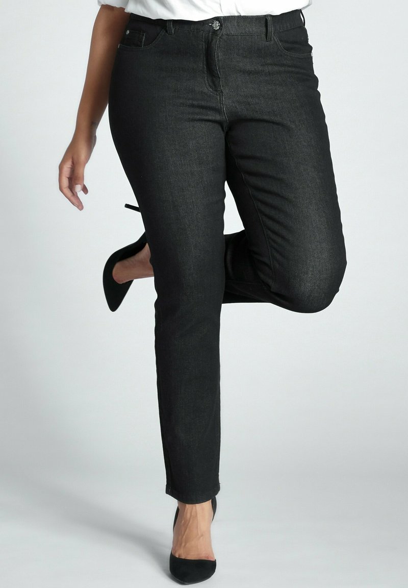 Jeans de mezclilla negros con un corte ajustado, que cuentan con cierre de botón, bolsillos frontales y una textura suave. Llevados con tacones altos negros.