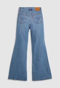 Jeans de mezclilla azul con acampanados y cintura alta, que presentan dos bolsillos traseros y un parche de cuero marrón en la cintura, exhibiendo un acabado texturizado.