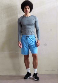 Sivý dlhý rukáv športový top s elastickým materiálom, kombinovaný s svetlomodrými šortkami s elastickým pásom, obutý s čiernymi športovými topánkami.