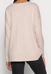 Jasnobeżowy sweter o luźnym kroju, z szerokim dekoltem i długimi rękawami. Miękka tekstura i prosty design, sięgający do bioder.